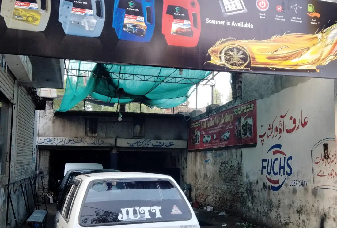 The lane into Arif Auto Workshop, with the shop's red banner and its name painted in Urdu on the wall